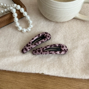 Detail showing two pink leopard print hair clips on a soft cream fabric background