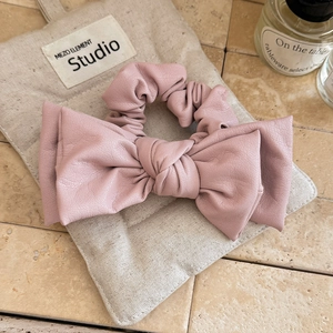 Detail showing soft pink faux leather bow hair tie texture on a linen fabric background
