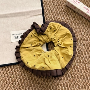 Detail of yellow polka dot scrunchie with brown lace edges on a textured background
