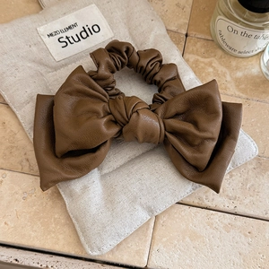 Detailed view of dark brown leather bow hair tie showing premium texture on burlap bag