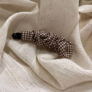 Detail of banana hair clip featuring brown and white gingham fabric with ruched texture