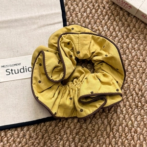 Yellow polka dot scrunchie with dark piping edge on textured woven background