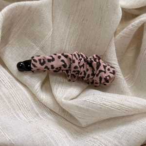 Close-up of leopard print fabric banana clip with elegant pleated texture on cream base