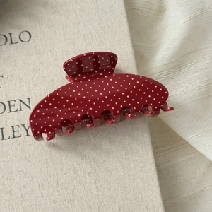 Macro detail of a red acetate hair claw clip with white polka dots on vintage paper
