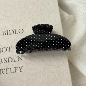 Close-up of a vintage black hair claw clip with white polka dots on a neutral background