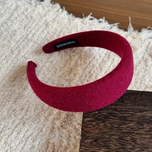 Deep red wool headband with handmade label shown on plush textured background