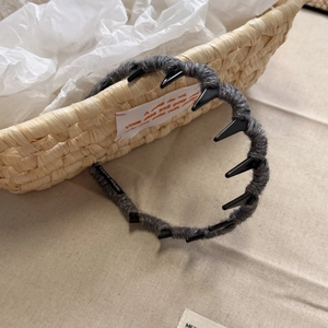 Detail of grey knitted headband with tooth comb and 'HAND MADE' label in a rustic setting