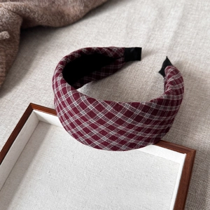 Close-up of red and white plaid fabric headband on a wooden tray with soft lighting