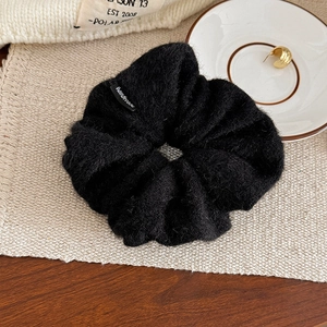 Détail d'un chouchou en laine noire pelucheuse avec une étiquette en tissu Handmade