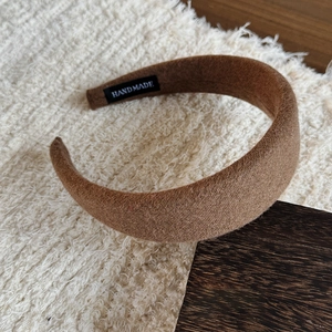 Detailed close-up of brown wool headband with handmade label on beige texture