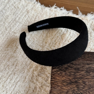 Detail view of a thick black velvet padded headband with a handmade label inside