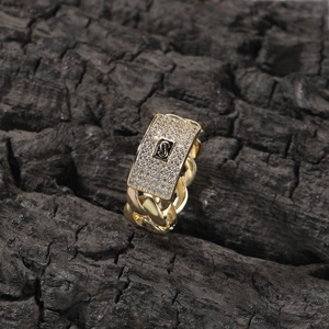 Macro detail of 14K gold Cuban link ring with pavé zircon setting and S logo center