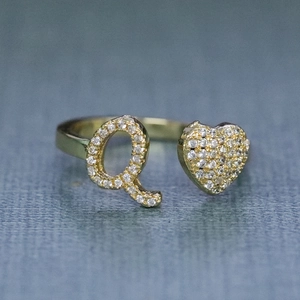 Vista macro di un anello regolabile in oro con lettera Q e cuore impreziositi da cristalli