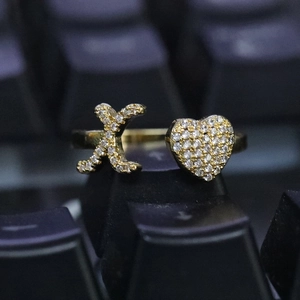 Dettaglio dell'anello dorato aperto con forme a X e cuore con pietre bianche incastonate