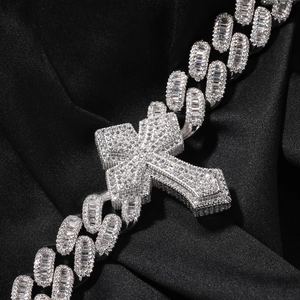 Close-up of iced-out silver cross pendant and thick Cuban link chain on black silk