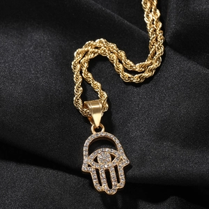 Macro shot of gold Hamsa hand pendant with pavé crystals on a black silk background