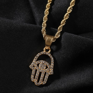 Close-up of golden Hamsa Hand pendant with white rhinestones on black satin fabric