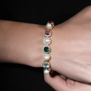 Macro shot of gold bracelet featuring colorful gemstones and pearls on a hand