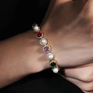 Elegant gold bracelet with white pearls and colorful gemstones worn on a model's wrist