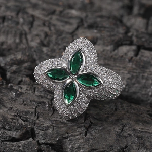 Funkelnder Kleeblatt-Ring mit grünen Zirkonia und weißen Pavé-Diamanten auf dunklem Holz