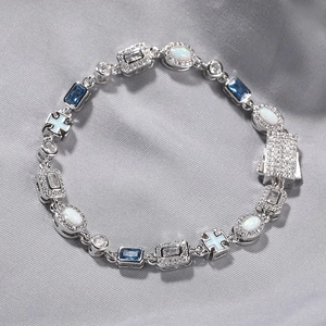 Detail of silver bracelet with blue gemstones, opal stones, and cross pendant on silk