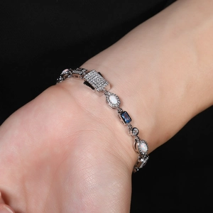 Detail of silver bracelet with blue gemstones and white opals on a dark sleeve