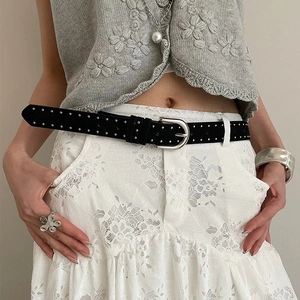Detail of a black suede rivet belt with silver metal buckle styled over a white lace dress