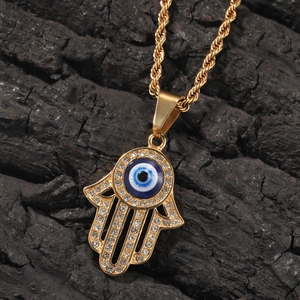 Macro del ciondolo mano di Fatima dorata con malocchio blu e cristalli su legno scuro