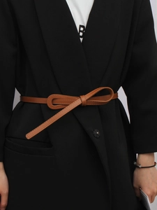 Vue détaillée d'une ceinture fine marron avec surpiqûres décoratives nouée sur un blazer