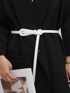 Détail d'une ceinture fine blanche avec surpiqûres élégantes nouée sur un blazer noir