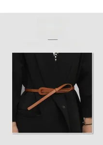 Ceinture fine en cuir marron nouée en nœud sur un blazer noir, détails de texture