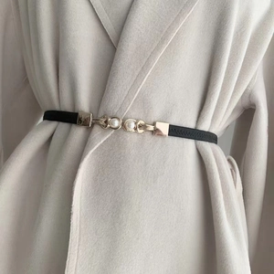 Detailed view of black elastic skinny belt with elegant gold pearl buckle on coat