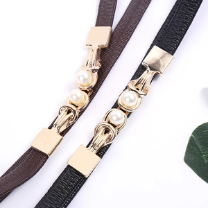 Close-up of elastic thin waist belts with gold metal buckle and dual pearl accents