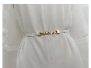 Detail of slim white elastic belt with gold pearl buckle on a white dress