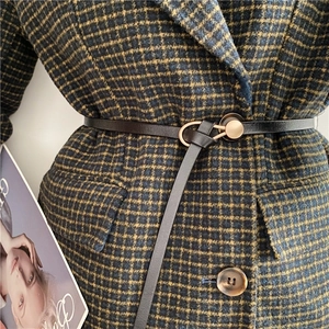 Detail of a thin black leather belt with a round gold buckle on a plaid coat