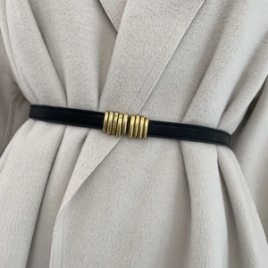 Dettaglio di una cintura sottile in pelle nera con fibbia dorata vintage su cappotto beige