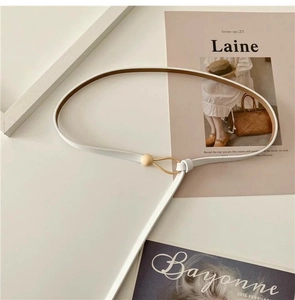 Detail of white cowhide leather belt featuring a round gold buckle and minimal design