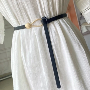 Detail of slim black belt with gold oval buckle styled on a white textured dress