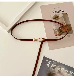 Minimalist brown leather thin belt for women with gold metal buckle on white magazine background