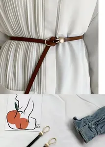 Detail of minimalist skinny belts with golden buckles shown on a white shirt and flat lay