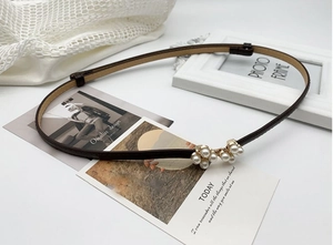 Détail d'une fine ceinture en cuir marron foncé avec boucle élégante en perles