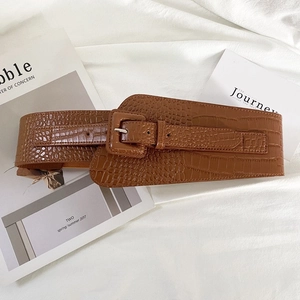 Détail d'une ceinture marron texture crocodile avec boucle carrée et bande élastique au dos