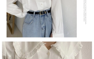 Détail d'une fine ceinture en cuir noir sur un jean taille haute avec chemisier blanc