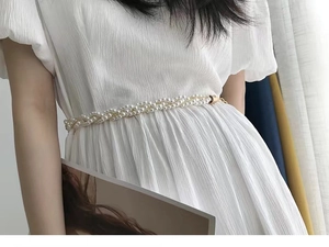Détail d'une chaîne de taille en perles tressées avec boucle dorée sur robe blanche