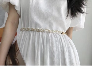 Détail d'une chaîne de taille en perles tressées avec fermoir doré sur robe blanche