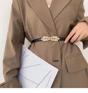 Detail of elegant black waist belt with gold leaf buckle worn over a brown blazer