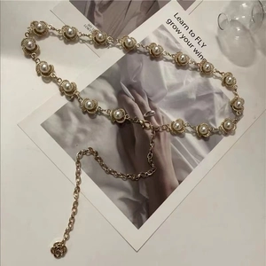 Detalle de cadena de perlas vintage con dijes de flores doradas sobre revista de moda