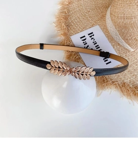 Close-up of elegant gold leaf buckle on slim black leather belt for dresses