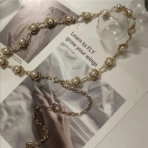 Detalle de cadena de cintura con perlas doradas y colgante de rosa en fondo minimalista