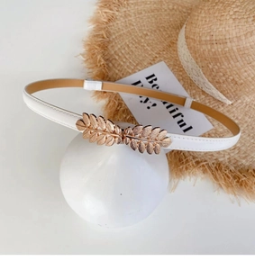 Detail of white leather skinny belt featuring golden leaf buckle on display stand
